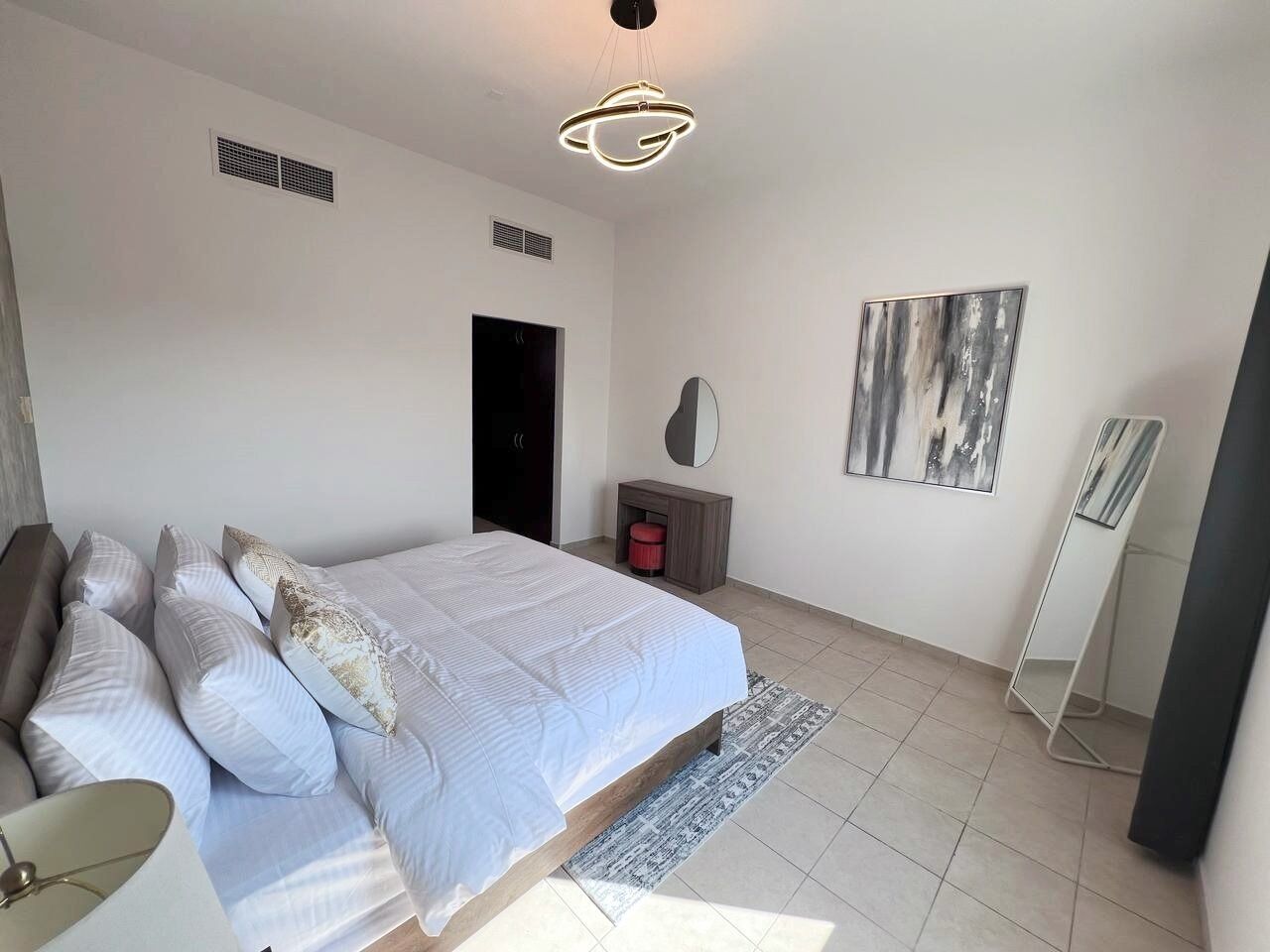 A bedroom with a bed, a bedside table, a mirror, a wall-mounted artwork, and a standing lamp.