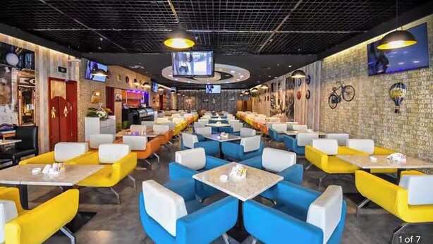 Un restaurante moderno con asientos tipo cabina en tonos amarillo y azul, una pantalla de televisión y una pared de ladrillo con ilustraciones de bicicletas y globos aerostáticos.