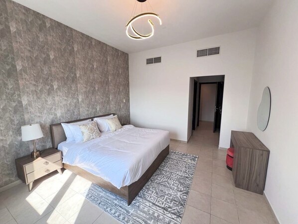 A modern bedroom with a large bed, a nightstand, a lamp, a patterned rug, and a wooden cabinet.