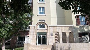 Un edificio de varios pisos con una entrada central, una escalera que conduce a la entrada y una placa con el número del edificio.