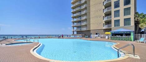 A swimming pool with a tiled deck, a tiki bar, and a high-rise building with balconies.