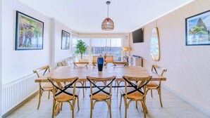 Un vaste espace dédié à la salle à manger, avec une grande table ronde, des chaises en bois et un luminaire suspendu.