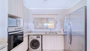 Une cuisine moderne dotée d’appareils électroménagers en acier inoxydable, d’un lave-linge intégré et d’une fenêtre donnant sur l’extérieur.