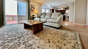 Un salon comprenant un canapé, une table basse, un tapis à motifs et une porte-fenêtre coulissante donnant sur un espace extérieur.