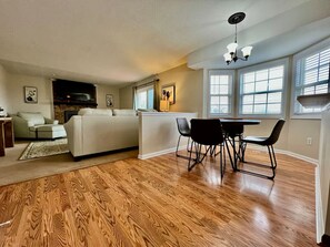 A living room with a sofa, a dining table with chairs, a fireplace, and large windows.