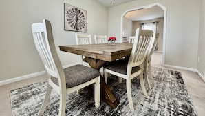 Une salle à manger avec une table en bois, des chaises blanches, un lustre et un tapis.
