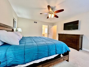 A bedroom with a bed, a ceiling fan, a dresser, and a TV on the wall.
