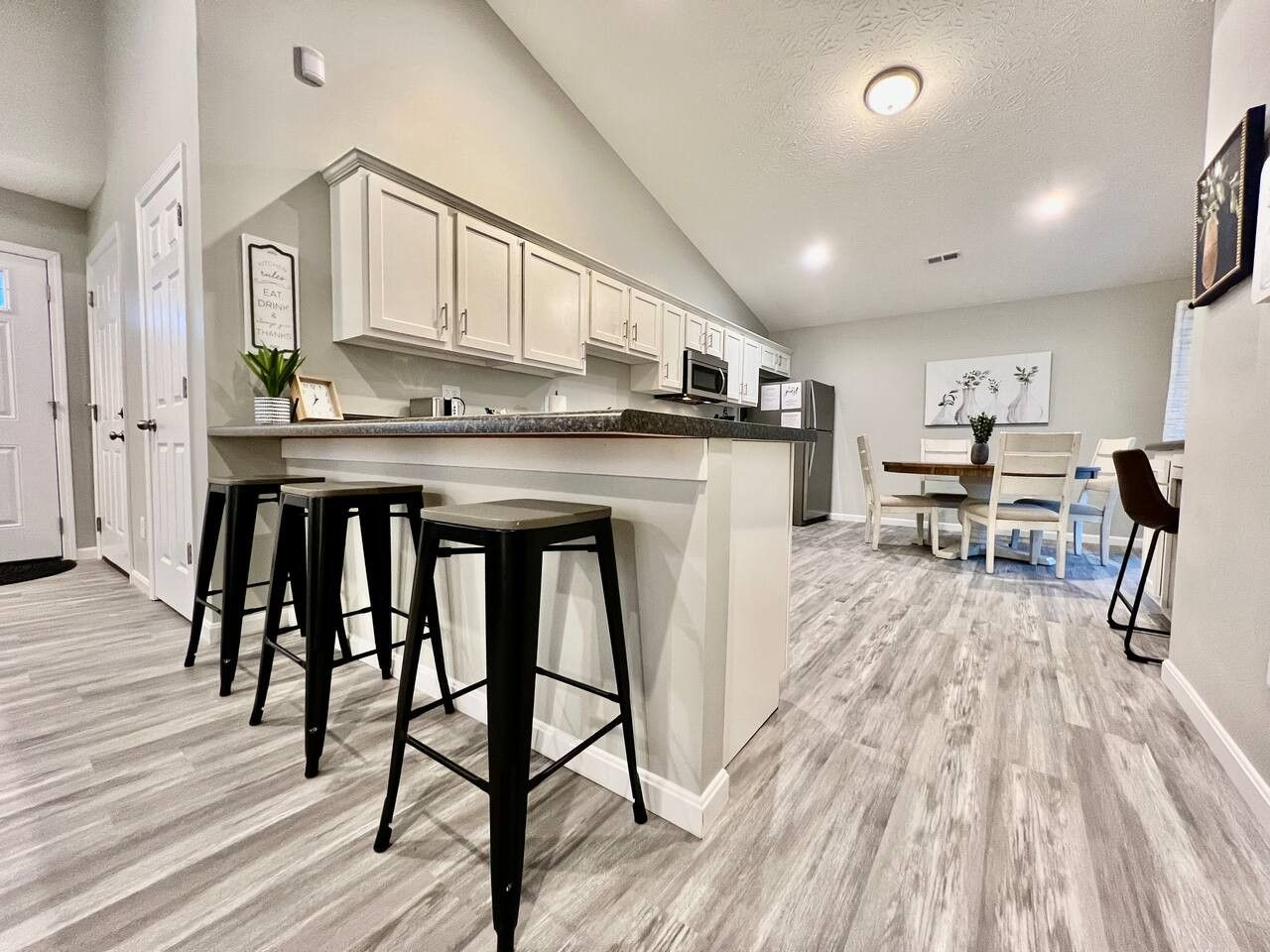 A kitchen with a central island, bar stools, white cabinets, and a dining area with chairs.