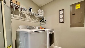 Une buanderie équipée de deux machines à laver, d’un étendoir et d’un panier à linge fixé au mur.