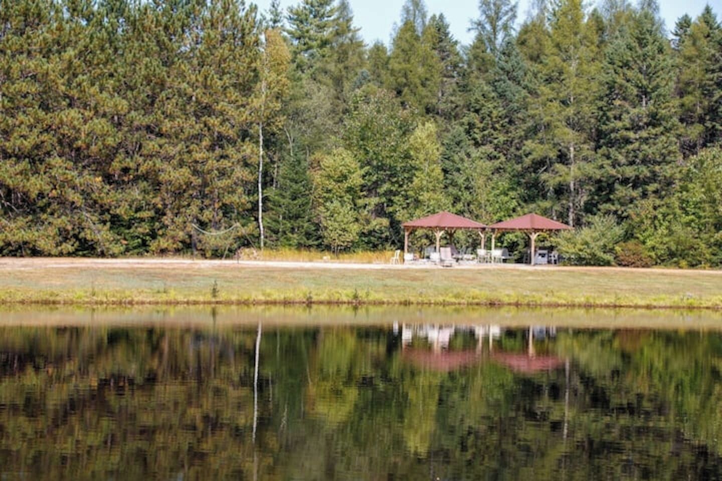 Un entorno tranquilo junto al lago con un pabellón y mesas de picnic, rodeado de un bosque denso.