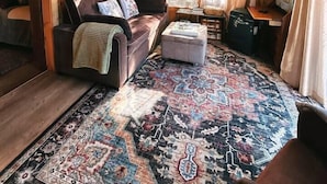 A cozy cabin interior with a wooden ceiling, a brown leather sofa, a patterned rug, and a small table. - Sunny Waterfront Cottage at FarAway Pond (Whitefield)