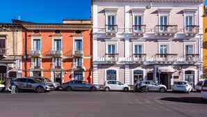 Une rangée d’immeubles à plusieurs étages, dotés de balcons, avec des voitures garées et un ciel bleu dégagé.
