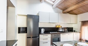 A modern kitchen with stainless steel appliances, white cabinetry, and a dining area with a glass table and woven placemats. - Klina Home by Wonderful Italy (Catania)