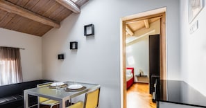 A modern, well-lit room with a glass dining table, a sofa, and a kitchen area. - Klina Home by Wonderful Italy (Catania)