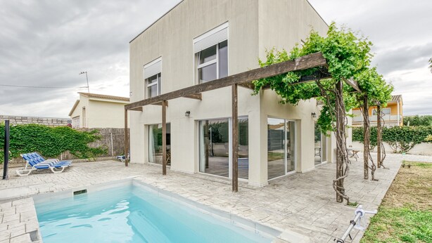 Een modern huis met een zwembad, een pergola begroeid met klimplanten en een terras.