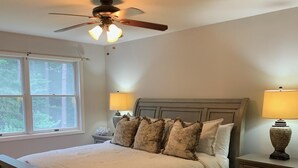 Une chambre à coucher avec un lit, deux tables de chevet, un ventilateur de plafond et une fenêtre.