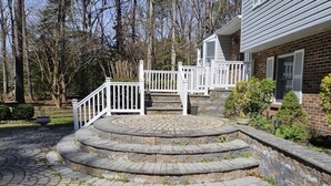 Un escalier en pierre mène à une véranda entourée d’une clôture blanche, avec une maison en briques en arrière-plan.