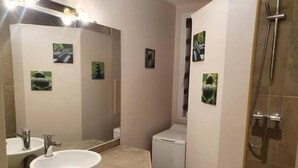 A bathroom with a white sink, a mirror, a toilet, and a shower. There are small pictures on the walls. - Ecully, Appartement au Calme de 50m² (Lyon)