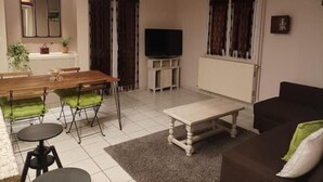 A living room with a dining table, chairs, a sofa, a TV, and a fireplace. - Ecully, Appartement au Calme de 50m² (Lyon)