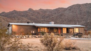 A modern, two-story building with a flat roof, large windows, and a satellite dish. It is situated in a desert landscape with mountains in the background.