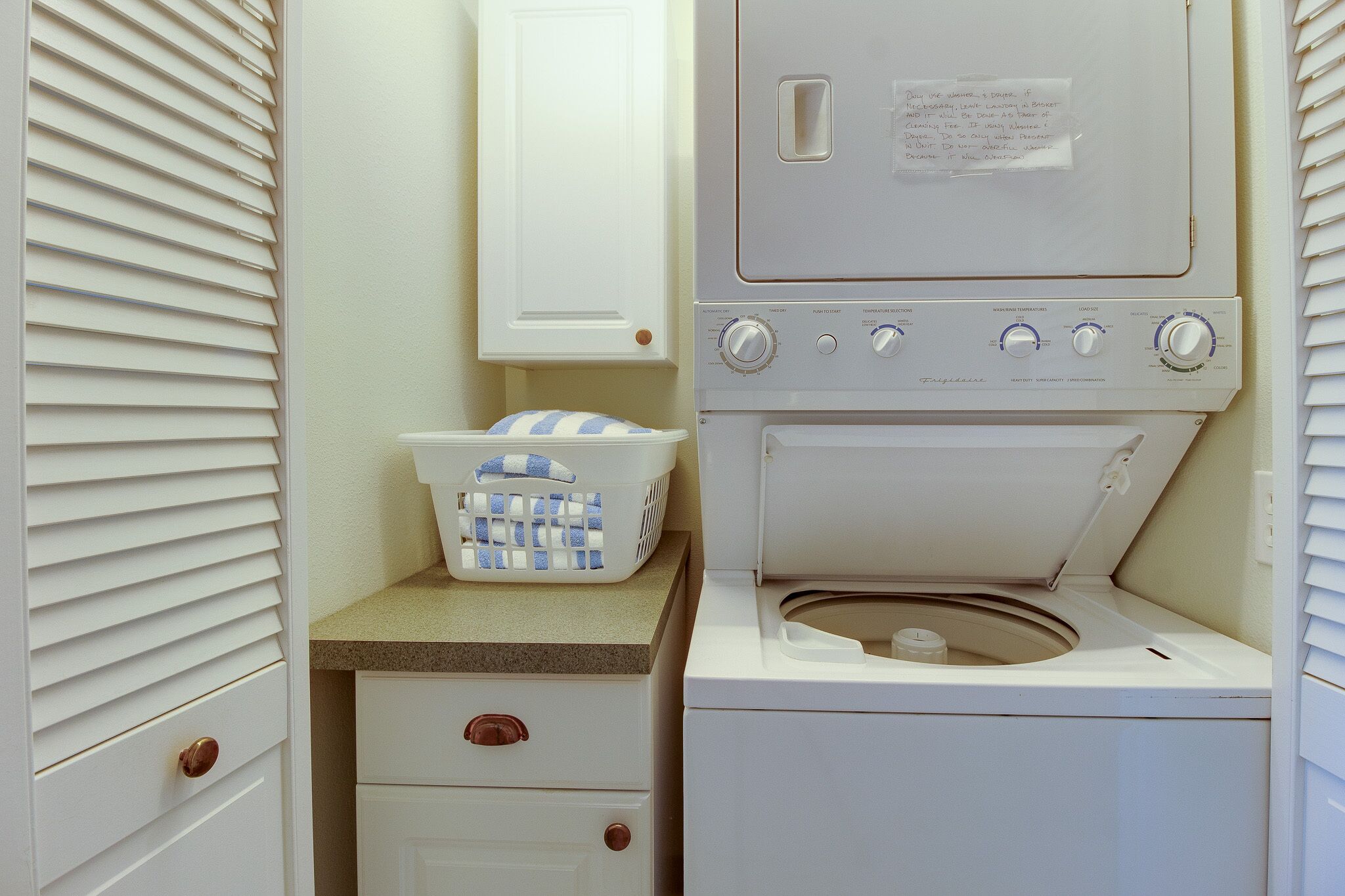 A compact laundry room with a washing machine, a dryer, a small countertop, and a basket.