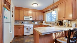 A kitchen with wooden cabinets, a white refrigerator, a microwave, an oven, a sink, and a large island with a chair.