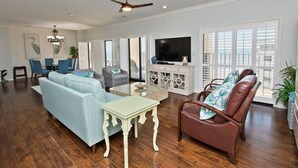 A spacious living room with a sofa, chairs, a coffee table, a TV, and a ceiling fan. - Summer Winds B-601, Oceanfront Condo in Indian Beach, NC! (Indian Beach)
