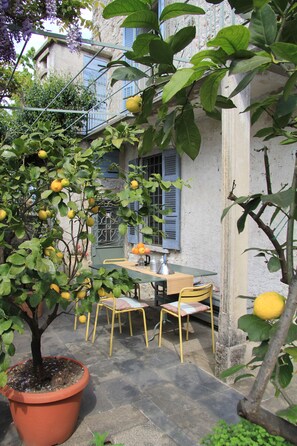 A courtyard with a table and chairs, surrounded by potted lemon trees and a building with blue shutters. - A 17th-century house with two stories, featuring a Turkish bath and courtyards, located 1 km from Lake Orta. (Monte San Giulio)