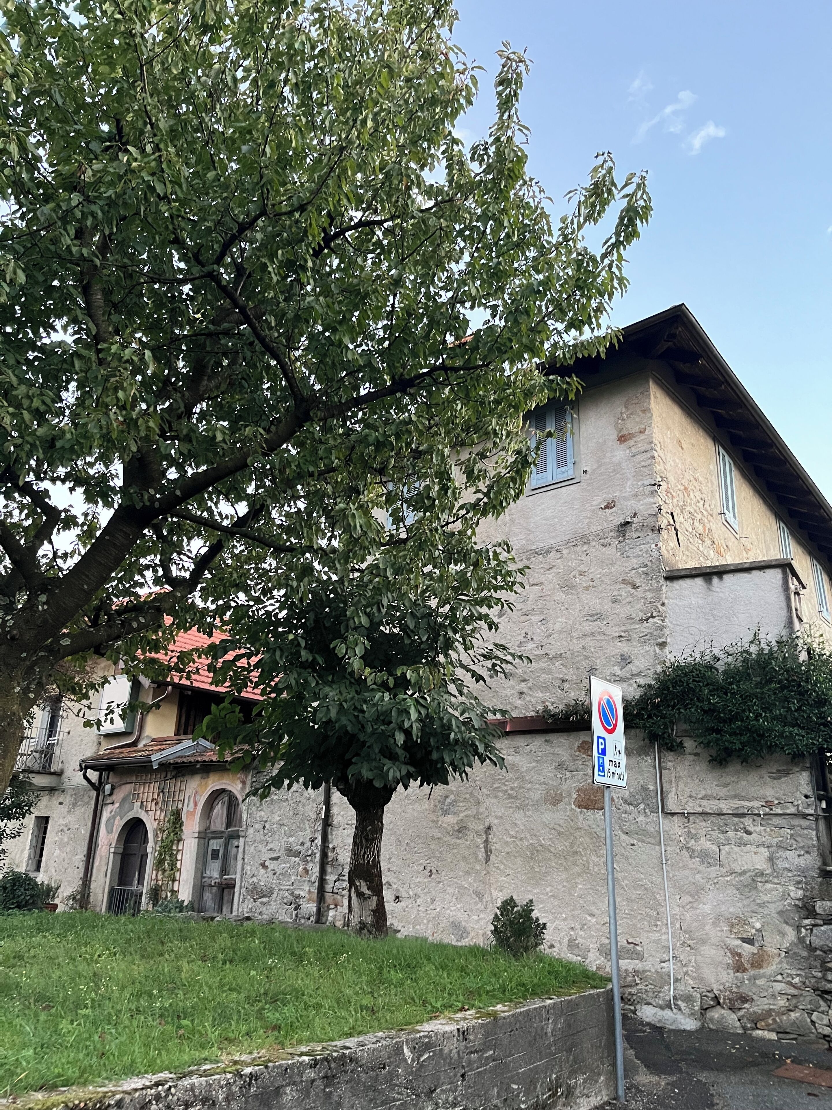 Edifício histórico com fachada de pedra, uma árvore em frente e placa de proibição de estacionamento.