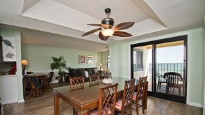 A dining area with a wooden table and chairs, a ceiling fan, and a view of the ocean through a sliding glass door. - Summer Winds A-402, Oceanfront Condo, in Indian Beach, NC! (Indian Beach)