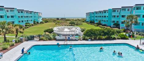 A swimming pool surrounded by turquoise buildings, with people swimming and lounging.