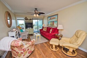 A living room with a red sofa, a beige chair, a television, and a painting of beach umbrellas.