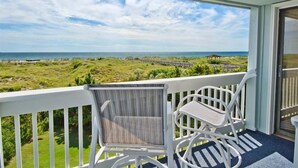 Ein Balkon mit Blick auf Strand und Meer, ausgestattet mit zwei weißen Stühlen und einem kleinen Tisch.