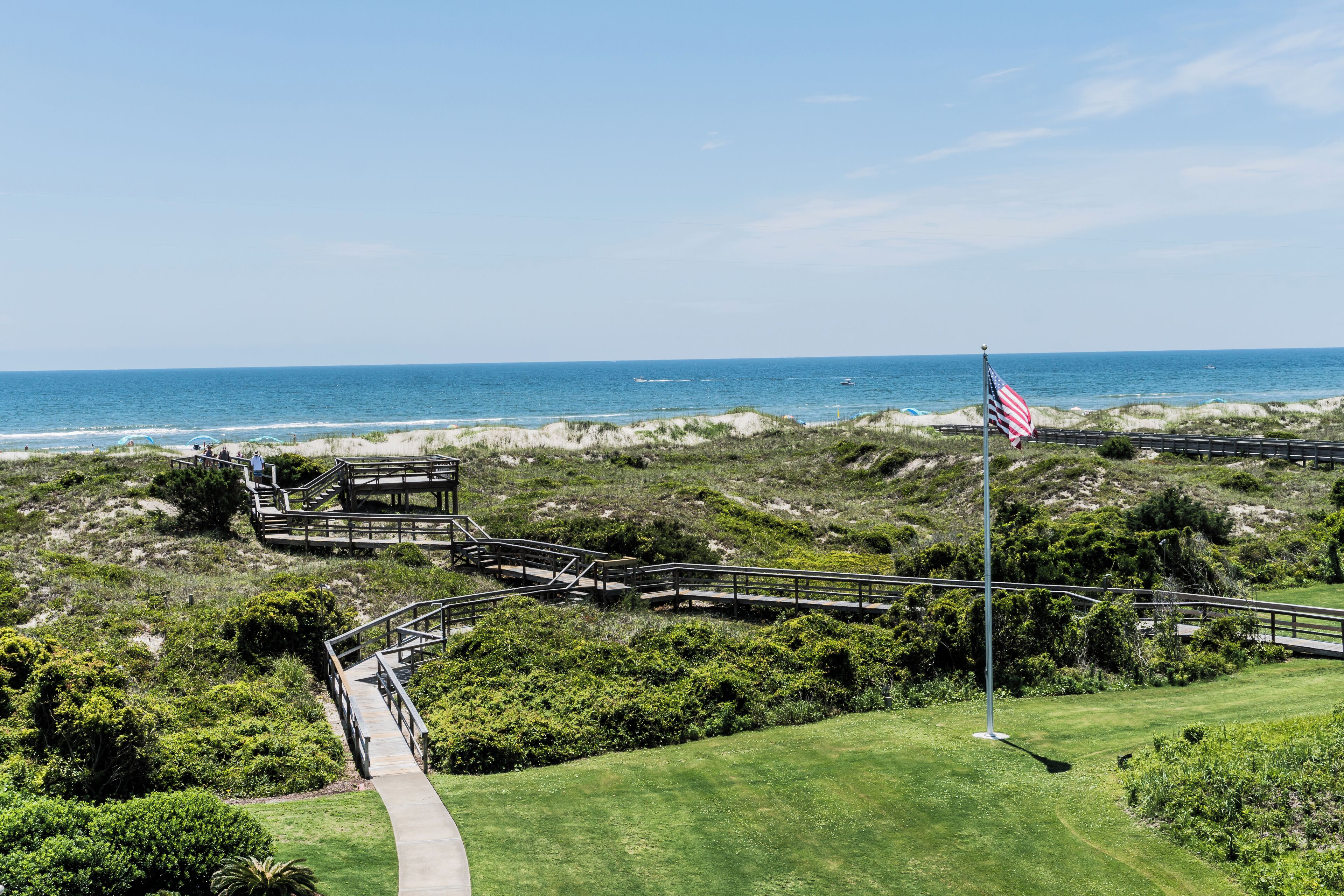 Un parcours de golf situé sur la côte, avec un pont en bois, un mât portant le drapeau américain et une vue dégagée sur l’océan.
