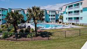 Ein mehrstöckiges, turkisanes Gebäude mit Swimmingpool, Palmen und Außenbereich.