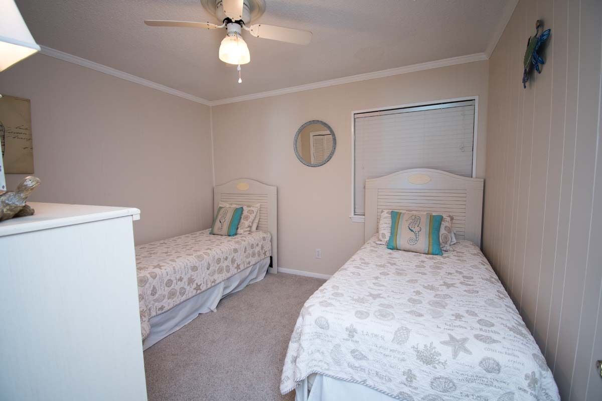 A bedroom with two single beds, a ceiling fan, a dresser, and a window with blinds.