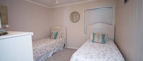 A bedroom with two single beds, a ceiling fan, a dresser, and a window with blinds.