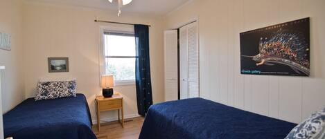 A bedroom with two beds, a ceiling fan, a window with curtains, a nightstand with a lamp, and a poster on the wall.