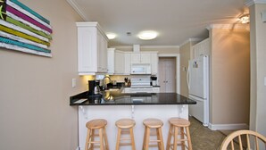 A kitchen with white cabinets, a black countertop, and three wooden stools. - Shangri La, Oceanside House in Emerald Isle, NC! (Emerald Isle)