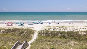 A beach with a wooden boardwalk leading to the shore, featuring beach umbrellas and sun loungers.