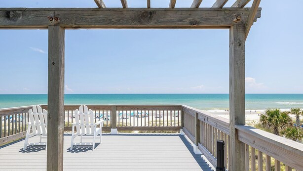 A wooden deck with white chairs and a view of the beach.