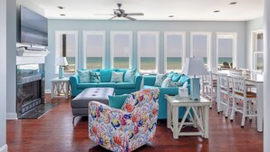 A spacious living room with a large window overlooking the ocean, a fireplace, and a dining area with white furniture.