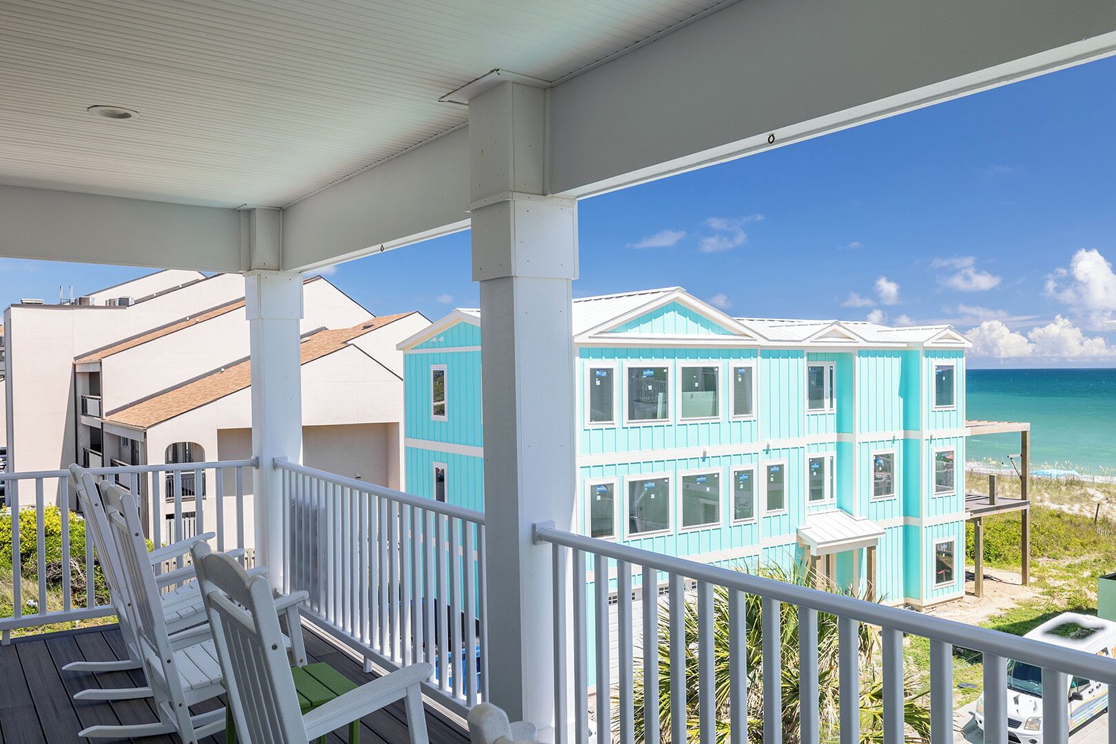 A turquoise two-story building with large windows, a balcony with white railings, and a view of the ocean.