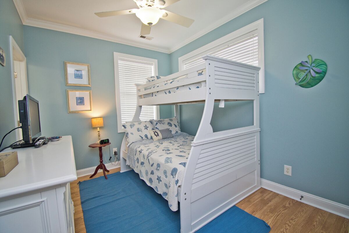 A child's bedroom with bunk beds, a desk, a lamp, and framed pictures on the wall.