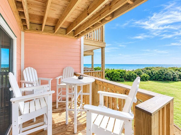 A wooden deck with white chairs and a table, overlooking a beach.