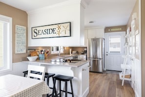 Una cocina con una isla central, armarios blancos, un refrigerador de acero inoxidable y un cartel que dice 'SEASIDE' con estrellas de mar.