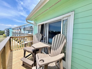 Une terrasse avec deux fauteuils Adirondack et une table, donnant sur un bâtiment à la façade verte et doté d’une porte-fenêtre coulissante.