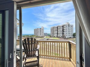 Ein Balkon mit Holzterrasse, einem Adirondack-Sessel und Blick auf mehrstöckige Gebäude und einen Strand.