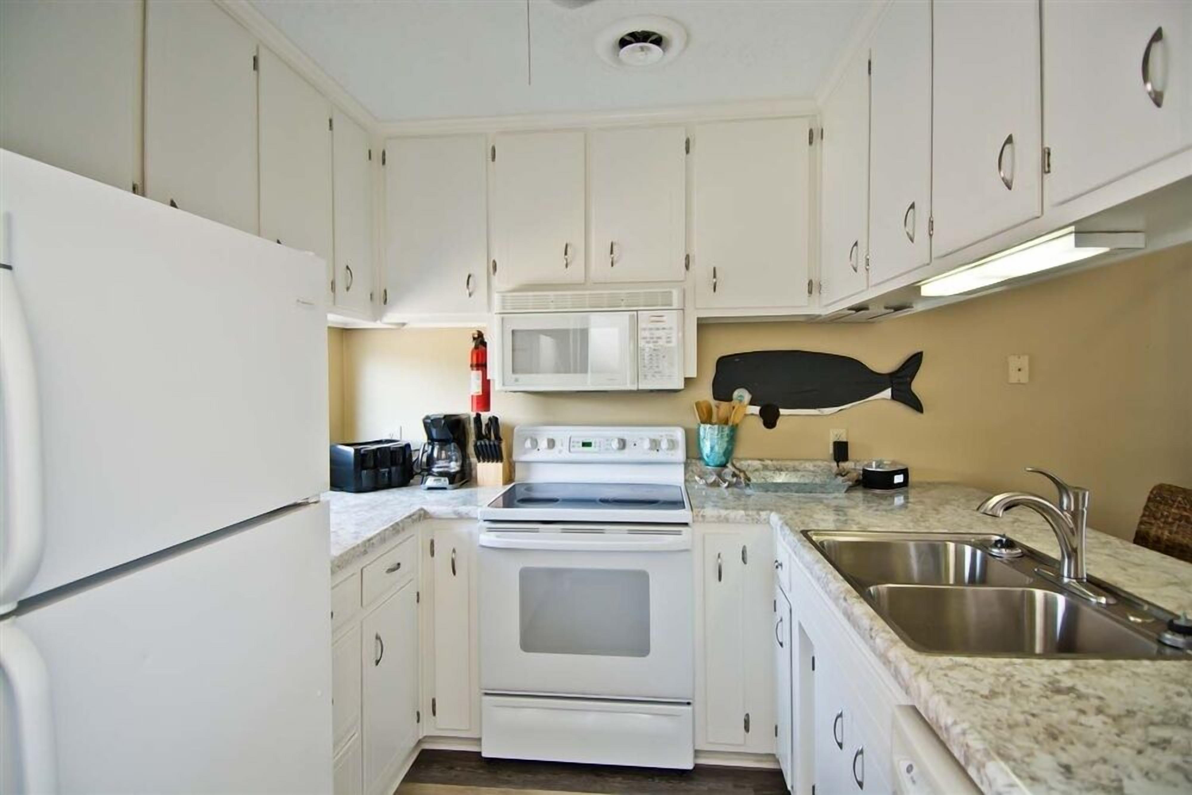 A kitchen with white cabinets, a microwave, stove, and a sink.