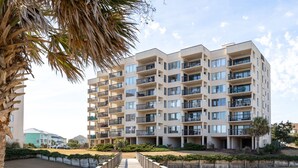 Un edificio residencial de varios pisos con balcones, una terraza de madera y cielo despejado.